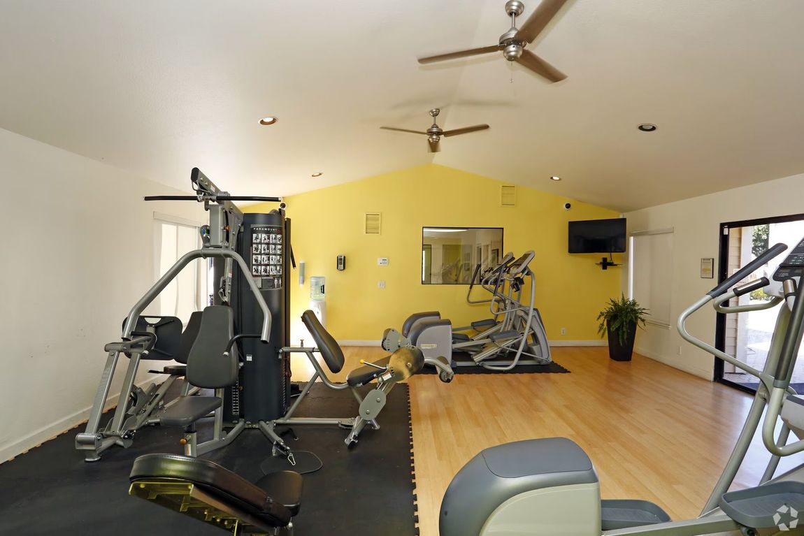 Empty gym room with exercise machines, yellow walls, wood floor, and ceiling fans