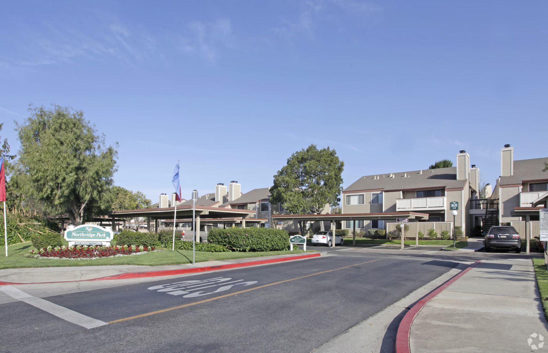 Apartment complex entrance with driveway, red curb, and clear blue sky
