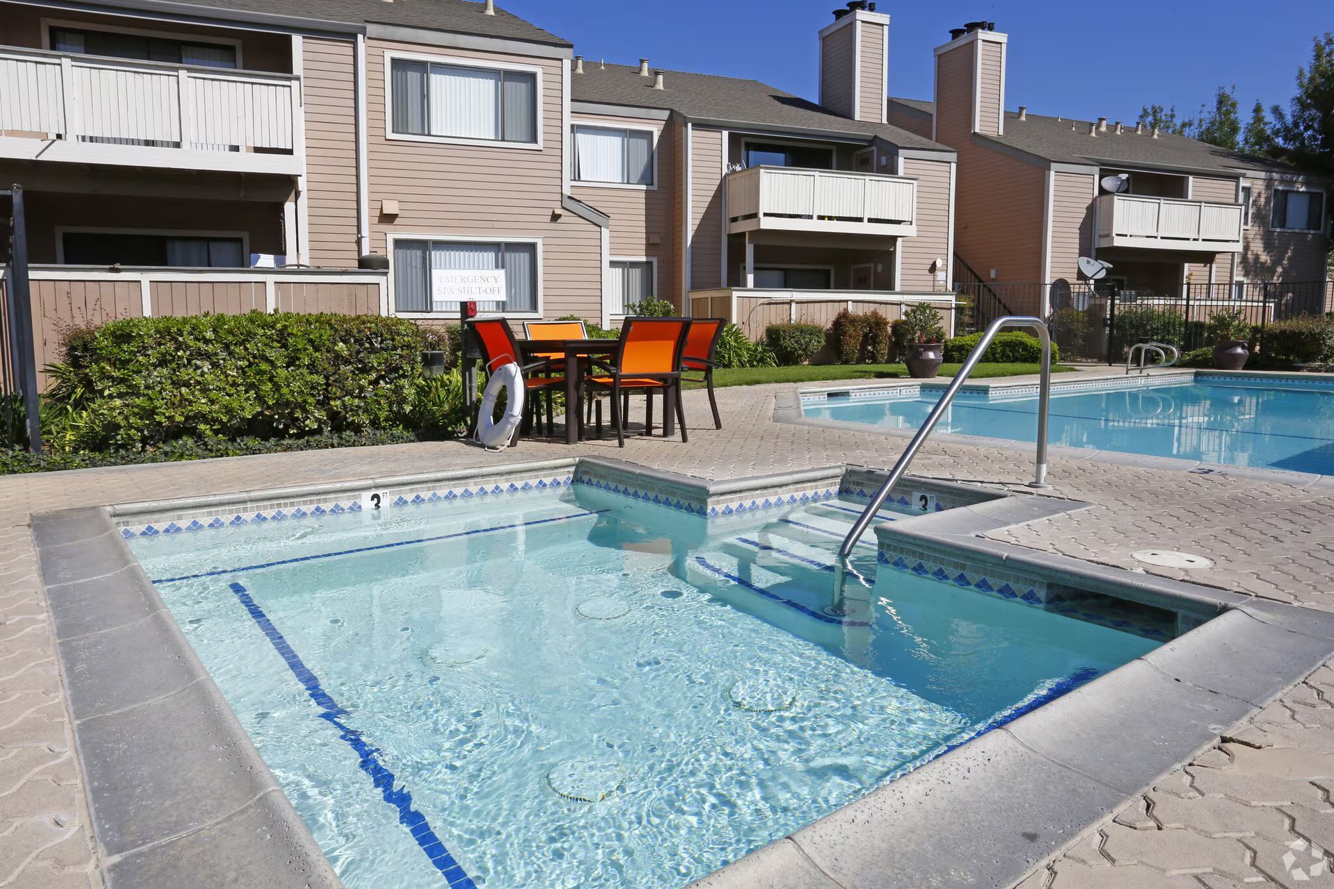 Apartment complex pool with a small hot tub and patio seating under a sunny sky