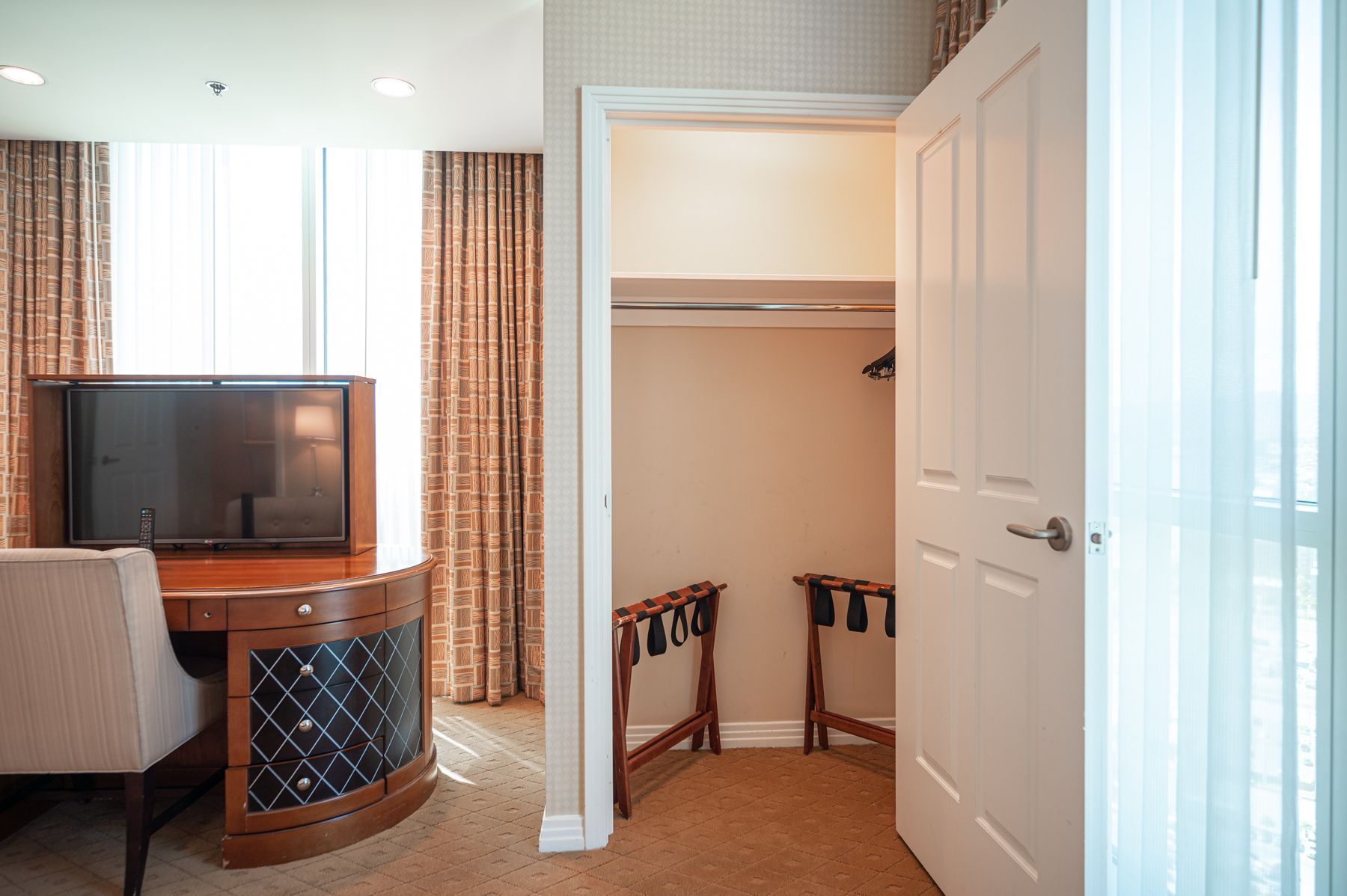 Hotel room with TV desk on left and open closet on right, lit by soft daylight
