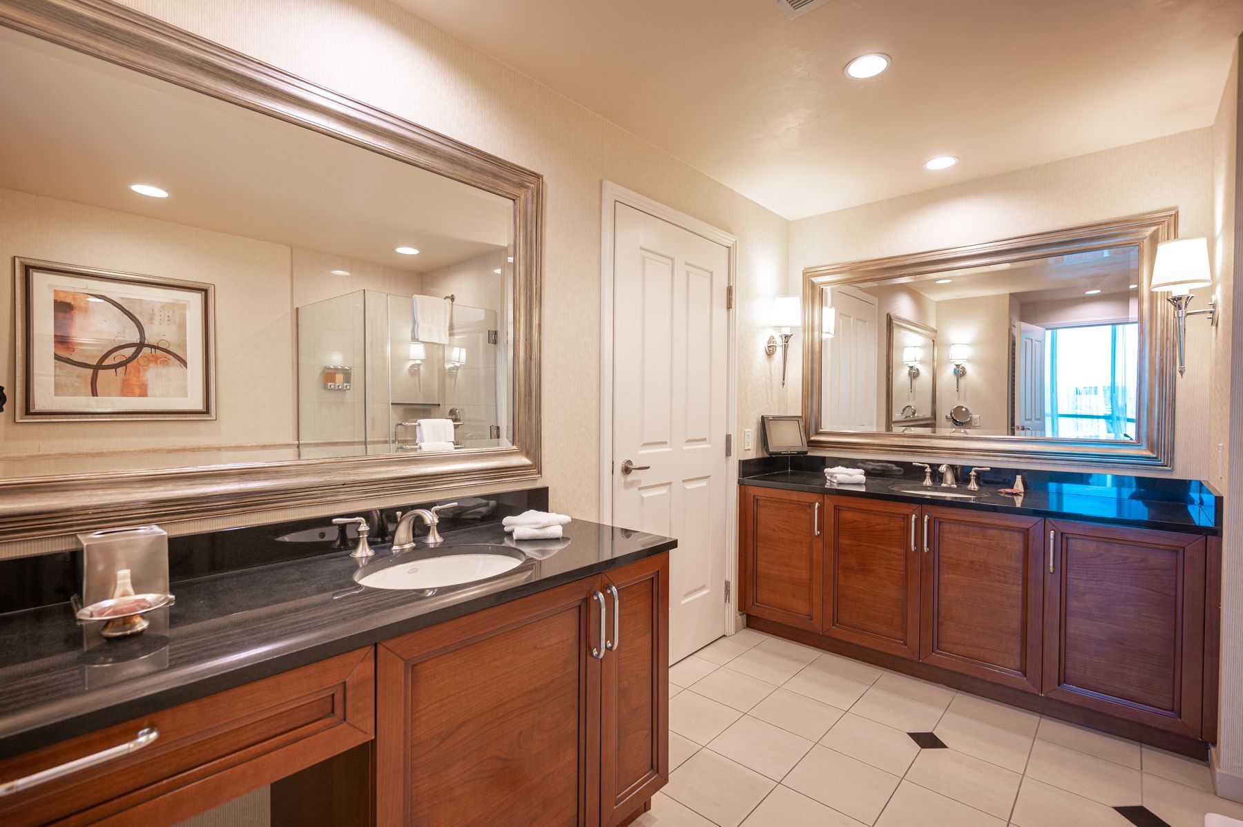 Modern bathroom with double vanity, large mirrors, granite counters, and warm wood cabinets