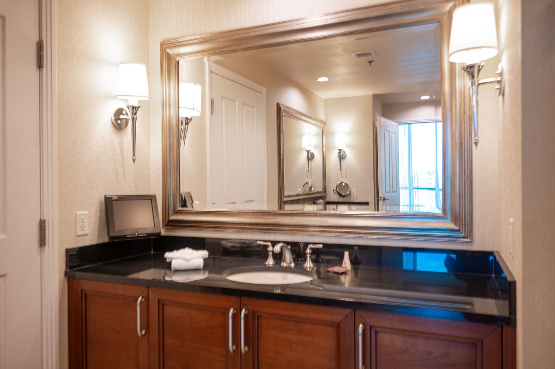 Bathroom vanity with large mirror, sink, dark countertop, and wall sconces.