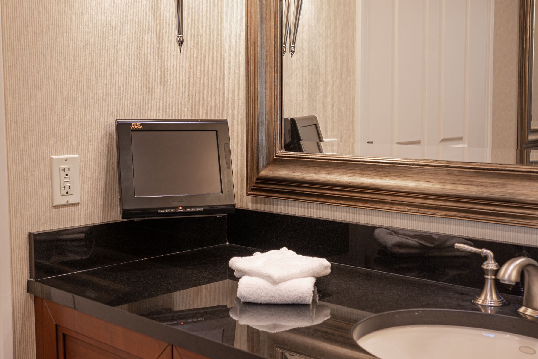 Hotel bathroom vanity with black countertop, sink, mirror, and folded white towels