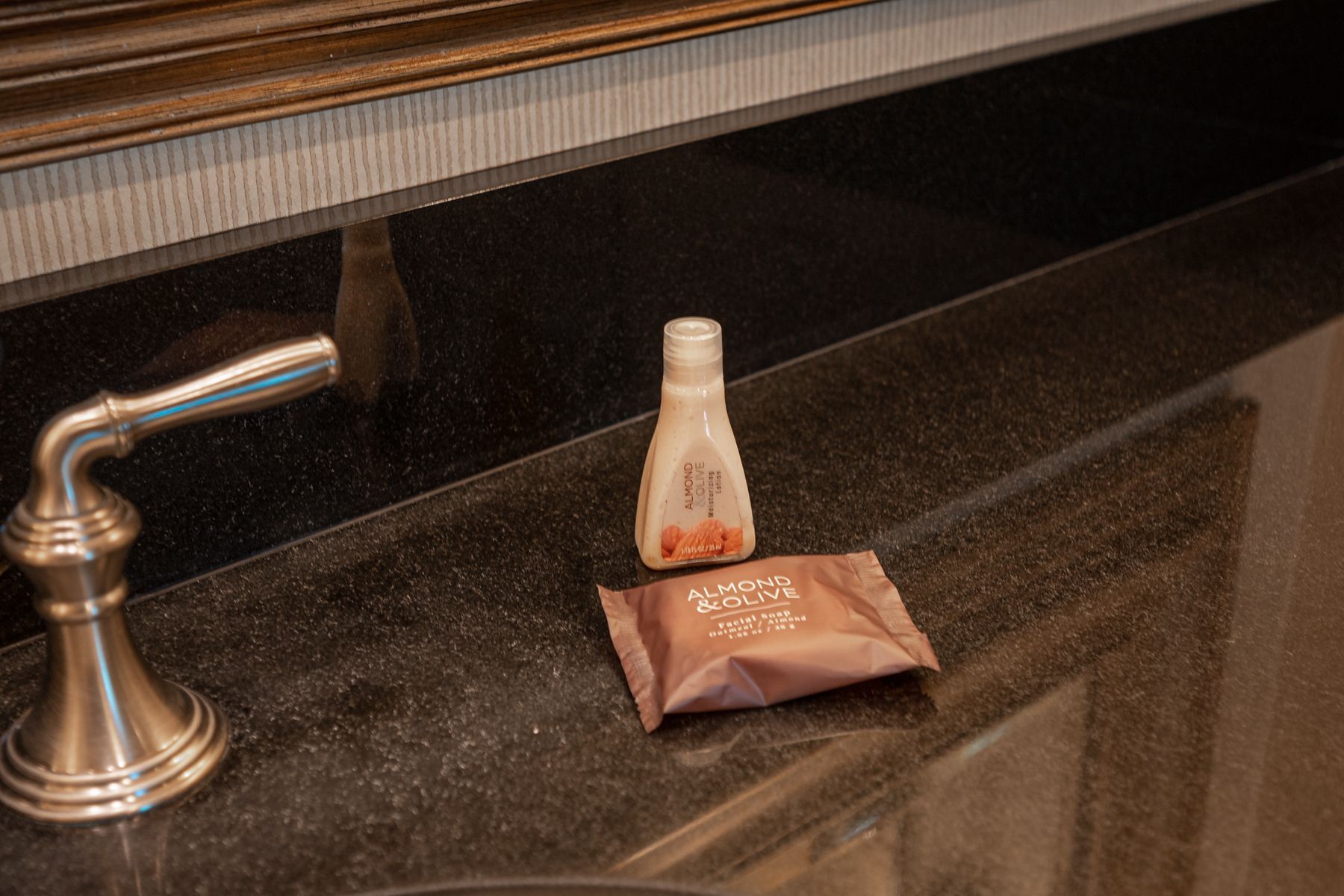 Small toiletries on a dark bathroom counter beside a sink faucet.