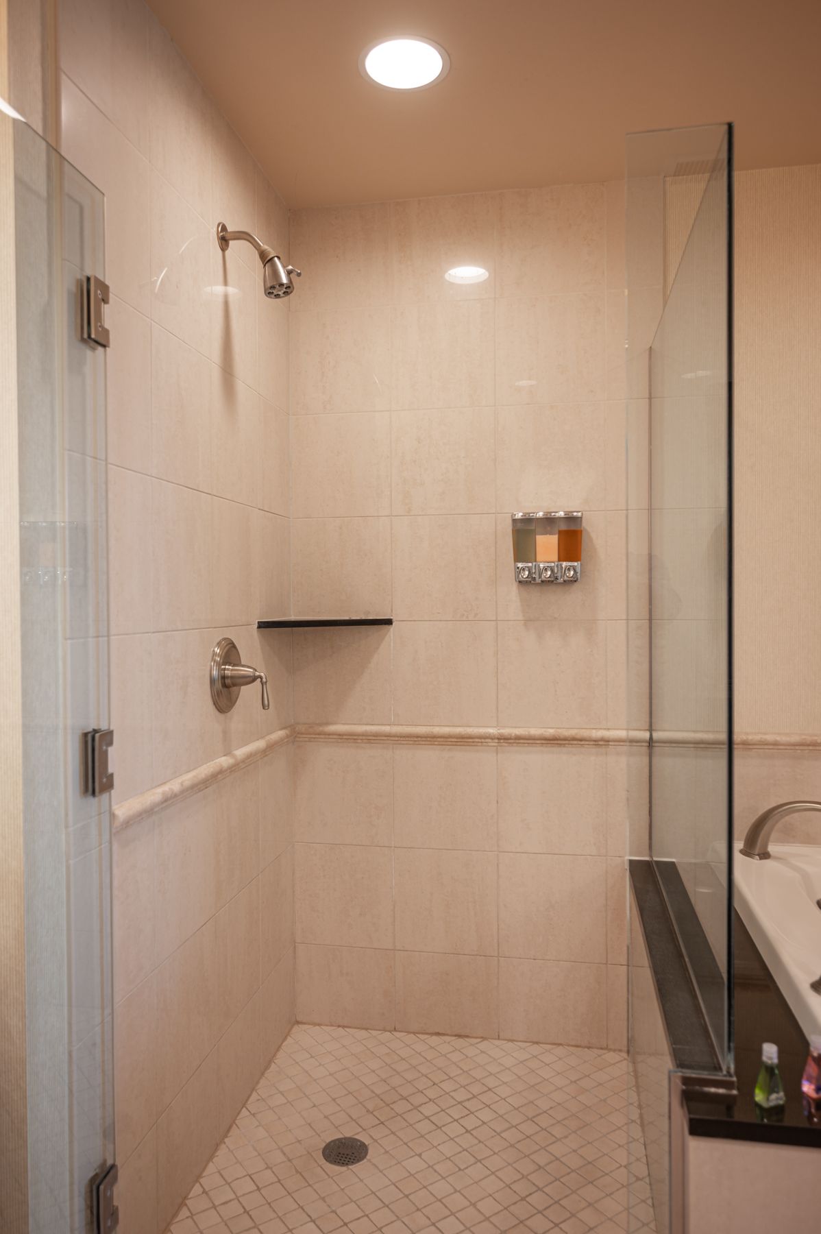 Modern bathroom shower with glass enclosure, beige tile, built-in shelf, and a dark bench.