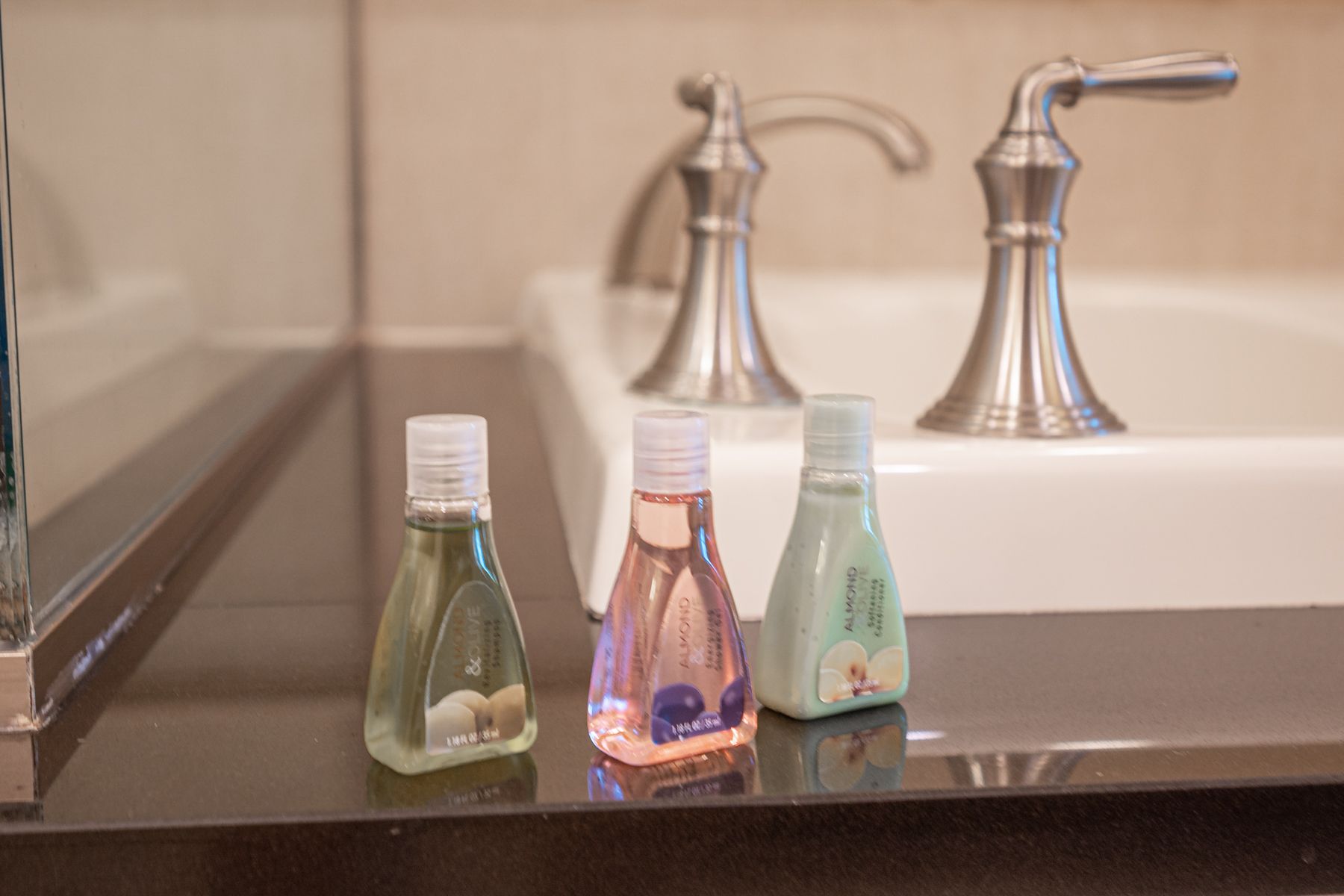 Three small colorful toiletries bottles on a bathroom counter beside a sink and faucet