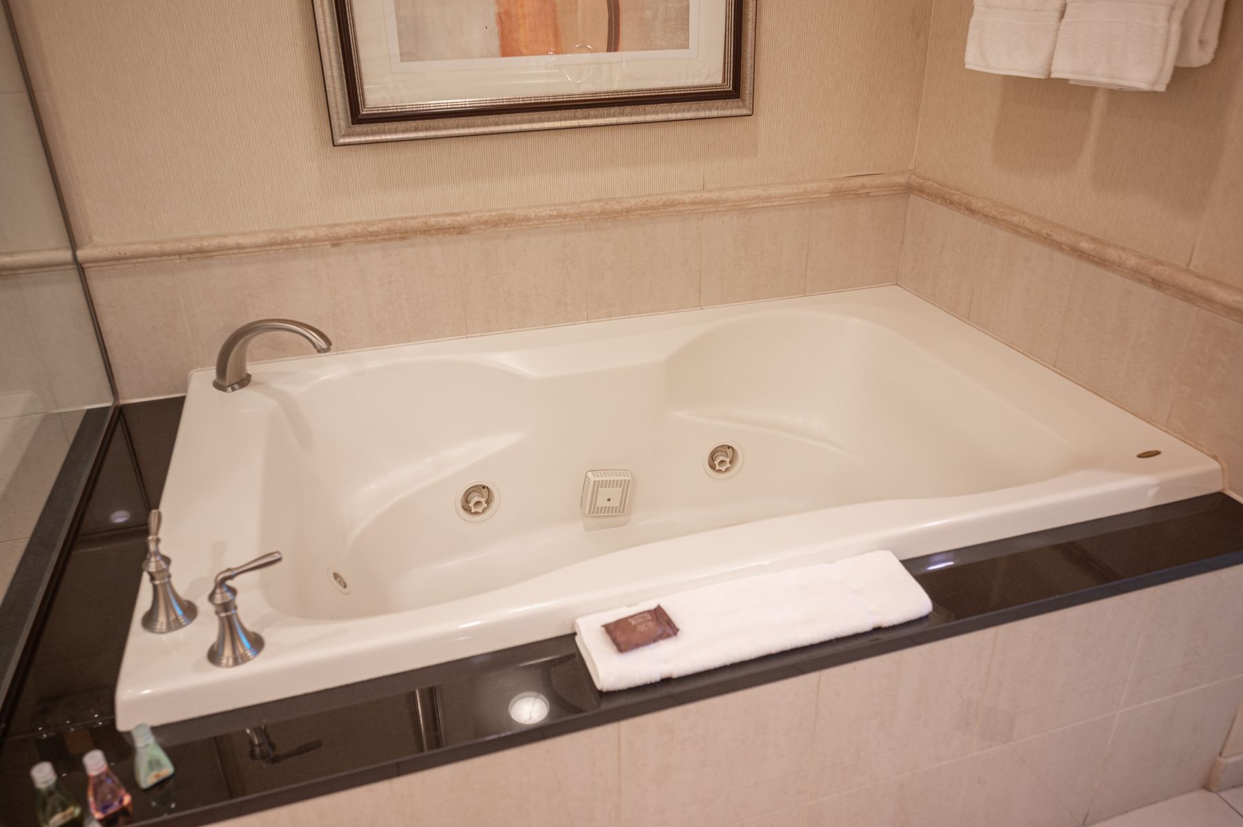 Empty white bathtub in a tiled bathroom with a window and ledge.