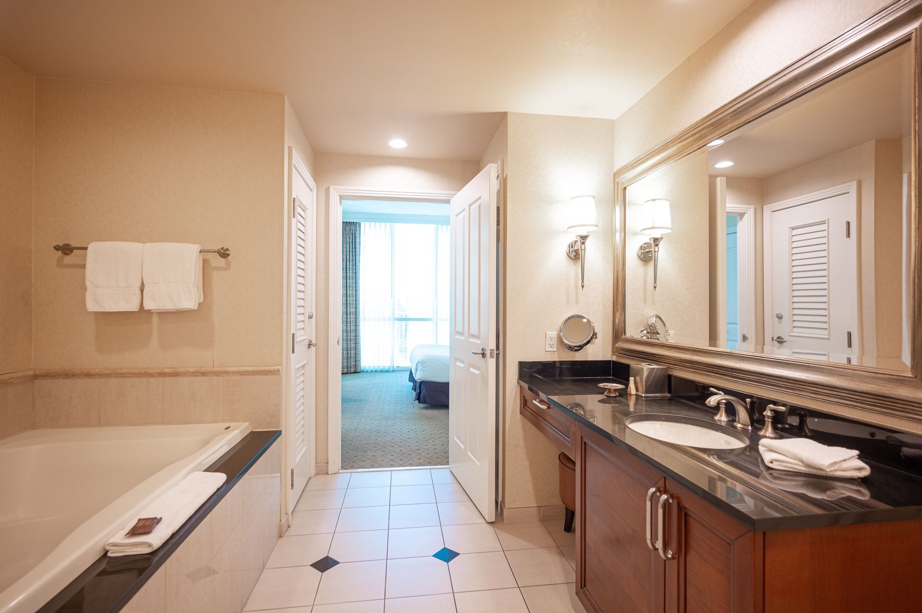 Luxury bathroom with bathtub, double vanity, large mirror, and tiled floor leading to a bright doorway