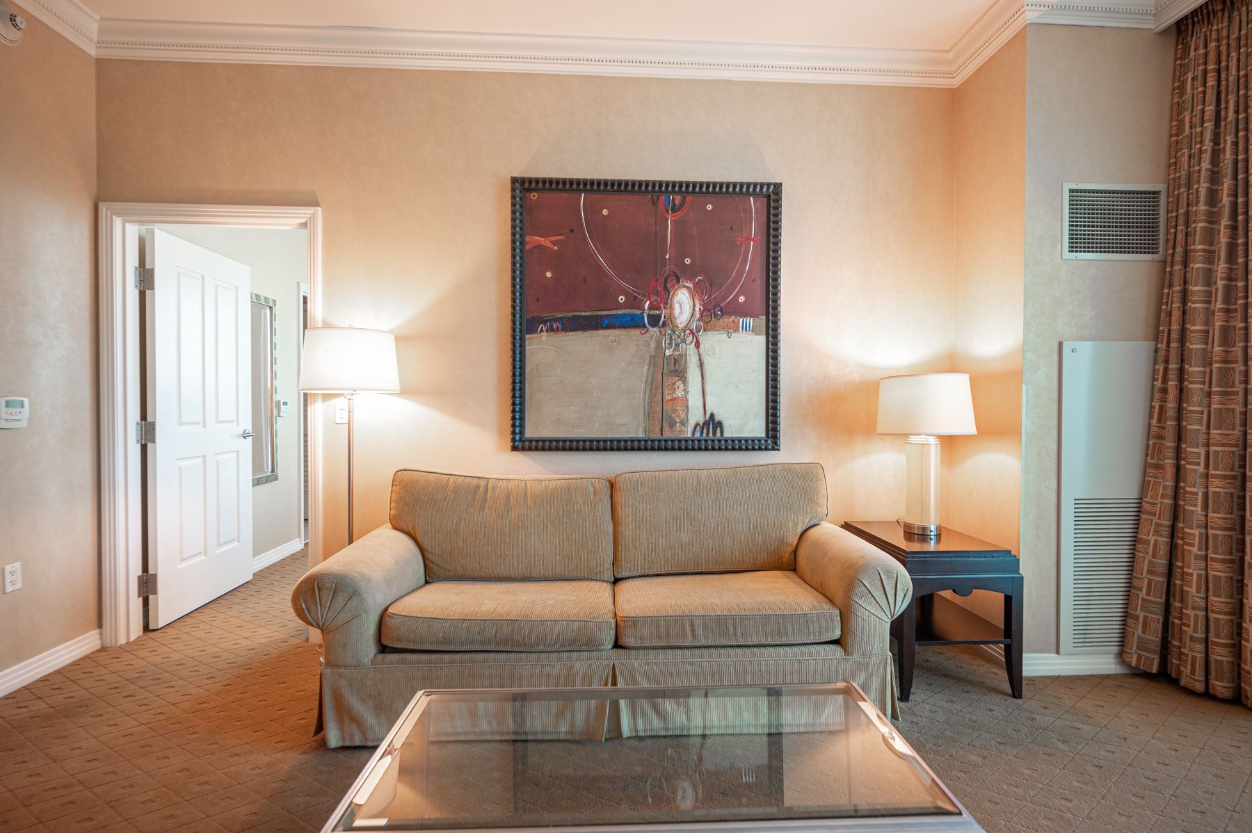 Living room with beige sofa, glass coffee table, lamps, and framed wall art