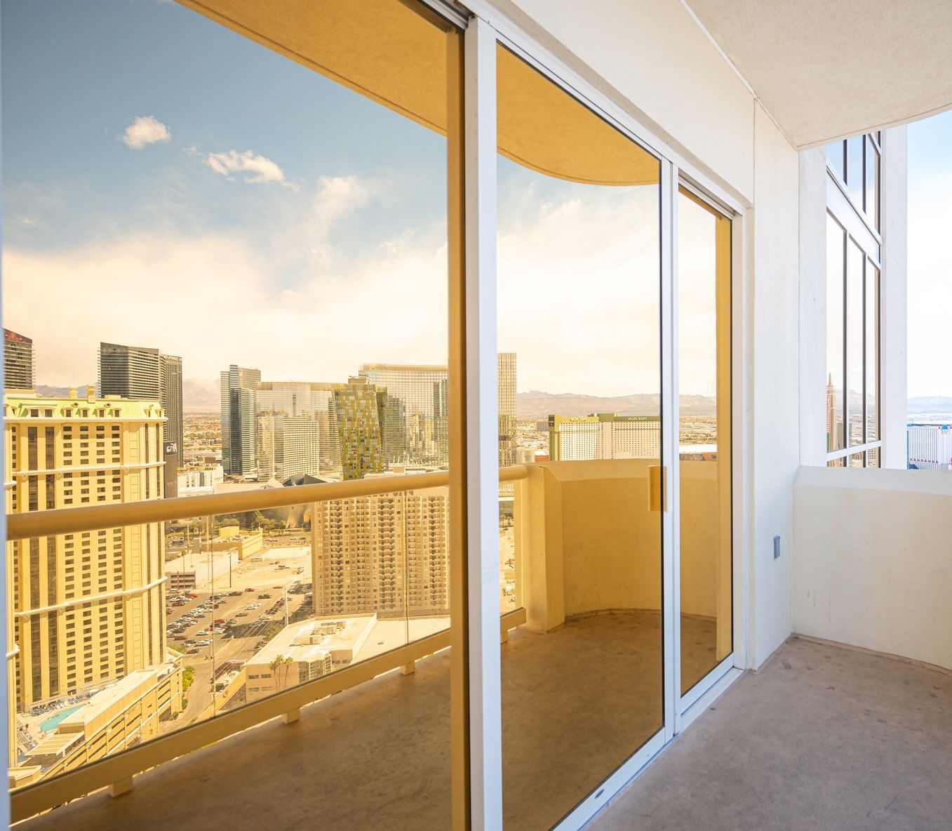 Sunlit balcony with sliding glass doors and a city skyline view at sunset