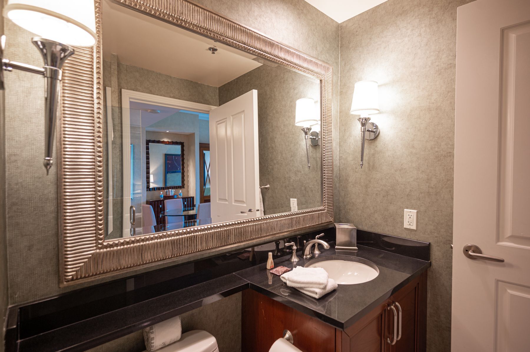 Small bathroom vanity with large framed mirror, dark countertop, sink, and wall sconce lighting.