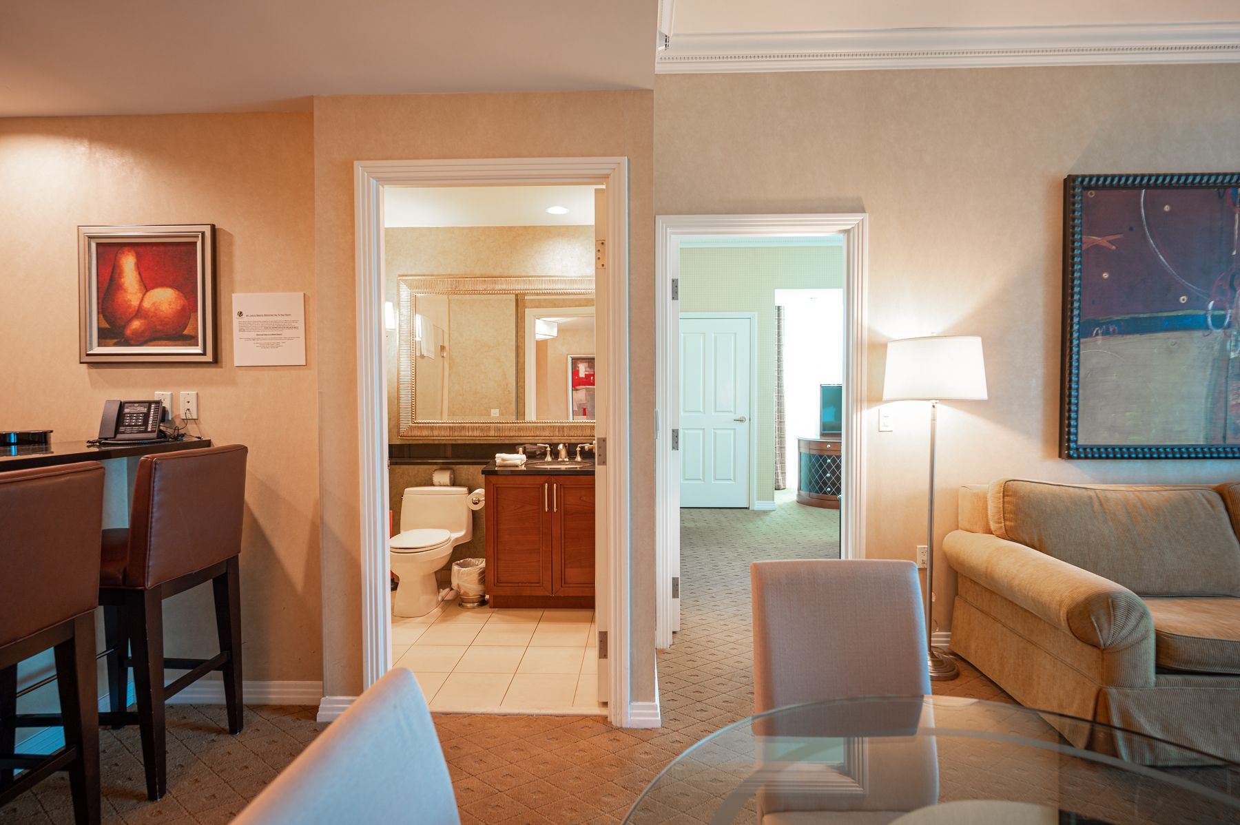 Cozy hotel suite with living area, open bathroom, sofa, lamp, and bar stools