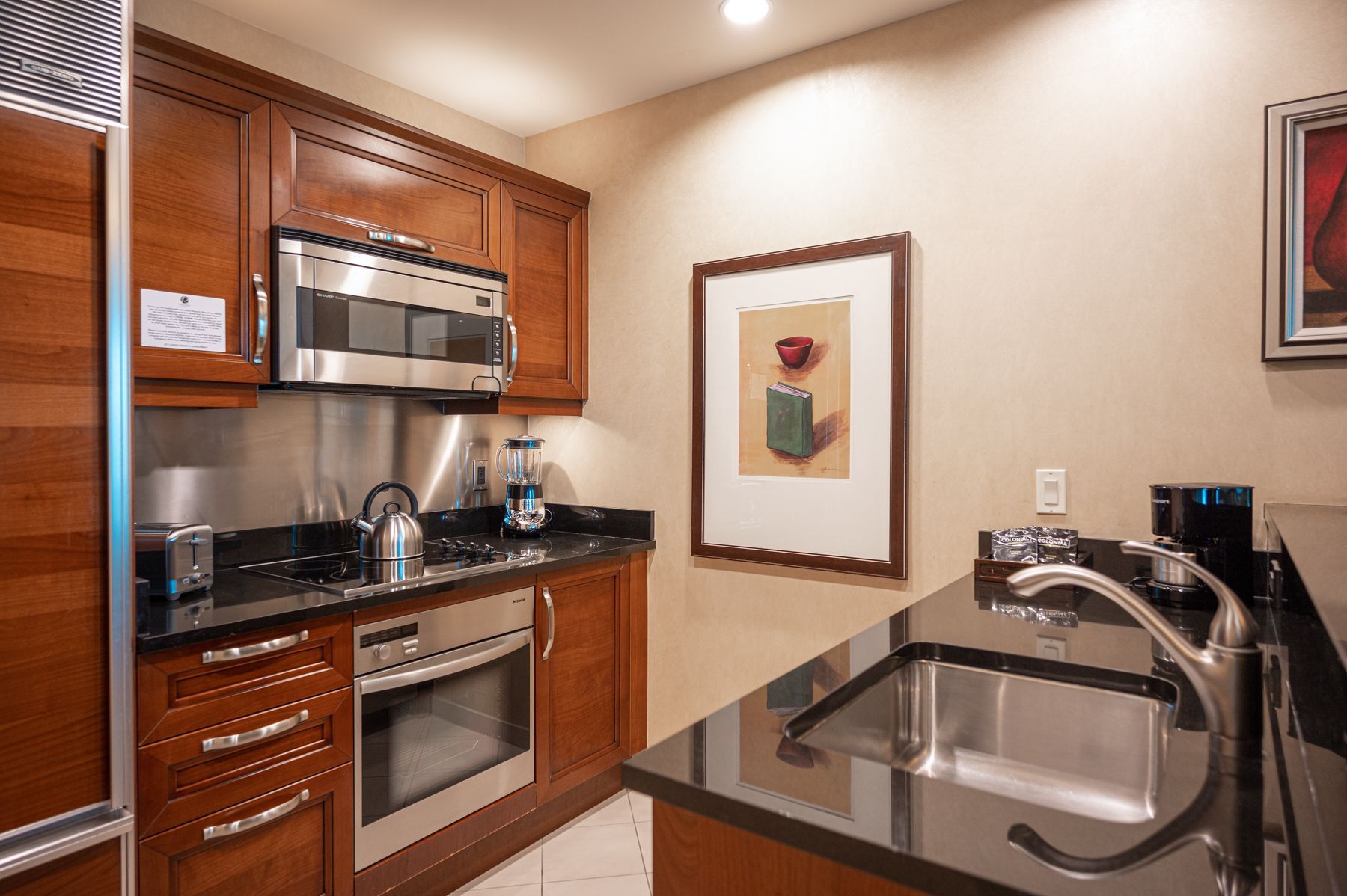 Compact kitchen with wood cabinets, stainless appliances, and a black countertop with double sink.