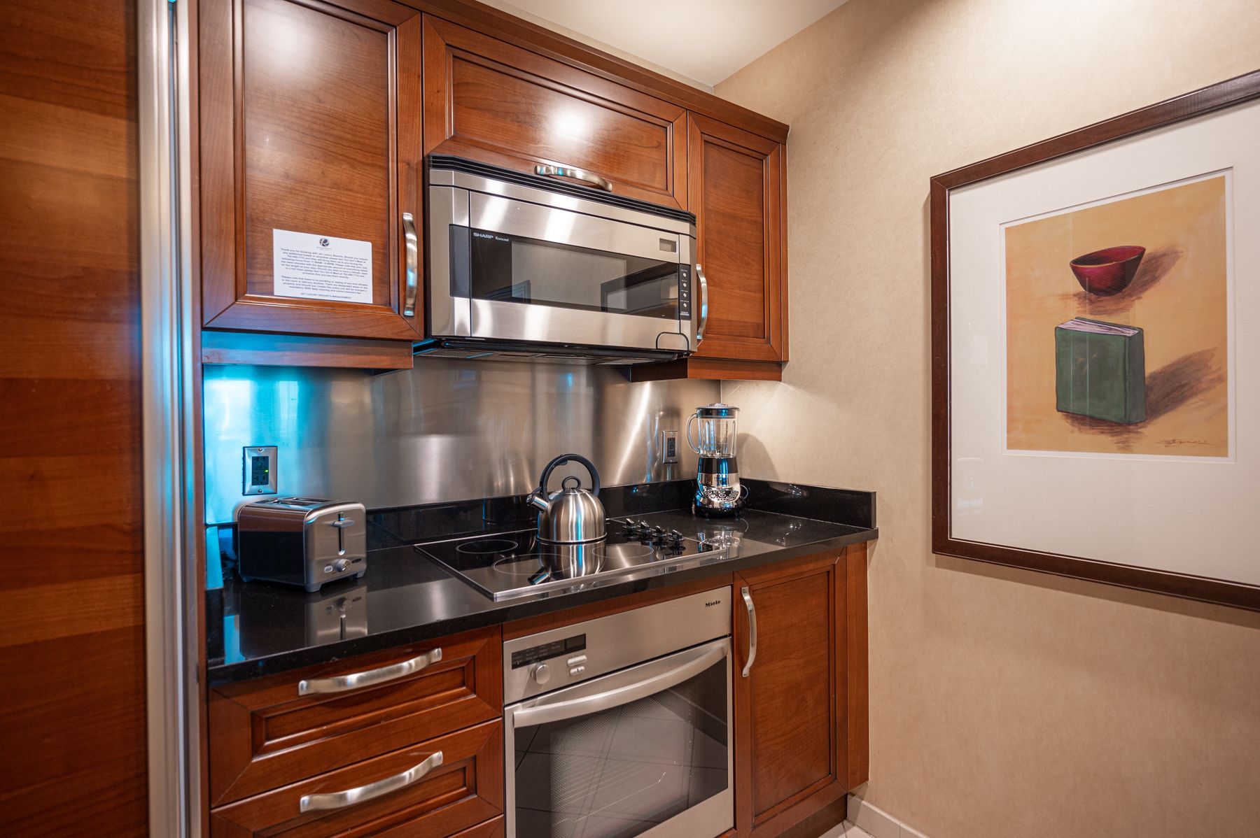 Compact kitchen nook with wood cabinets, black countertop, stainless microwave, sink, and small appliances
