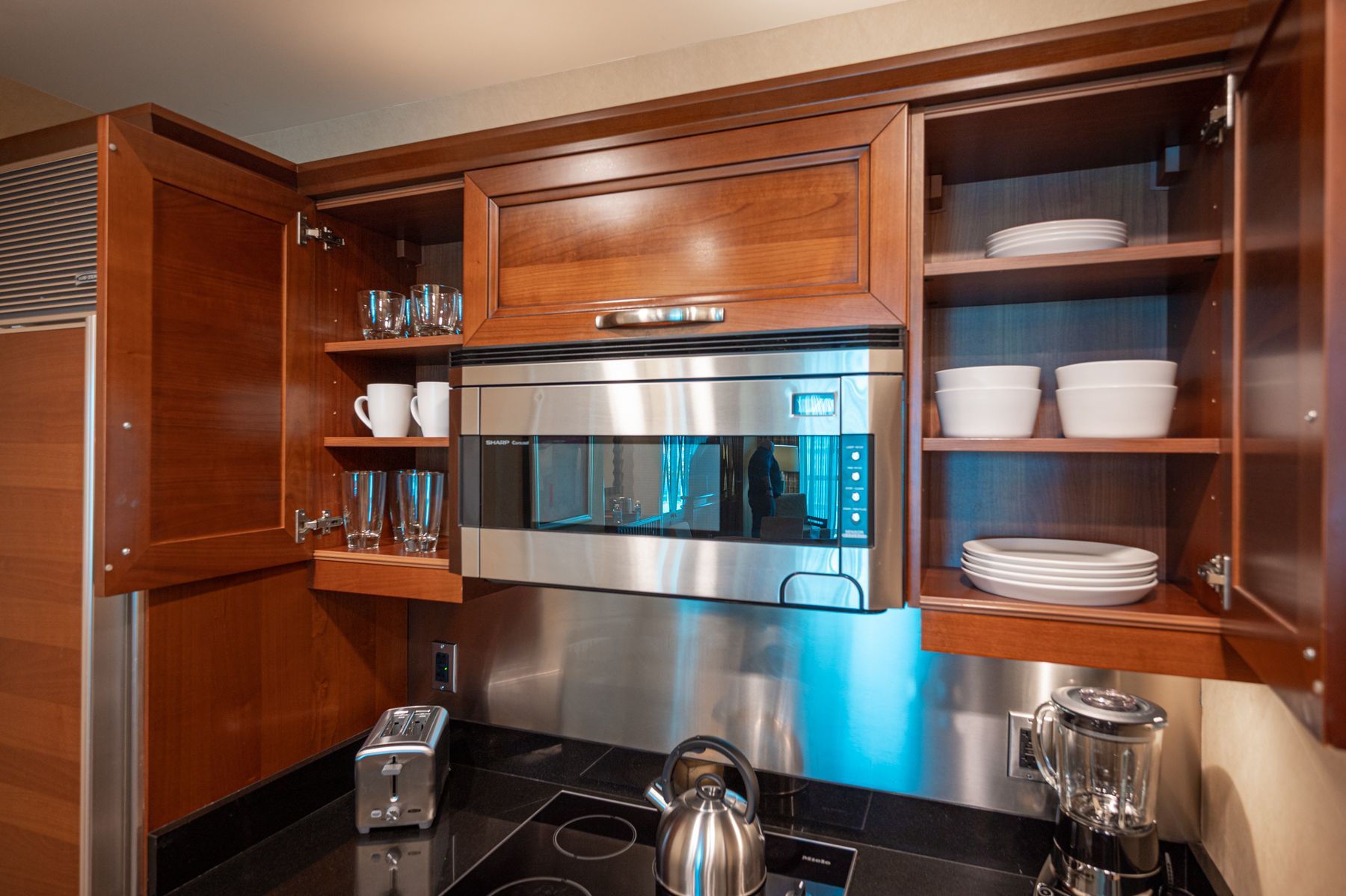 Wooden kitchen cabinets framing a stainless steel microwave above a black countertop with dishes and cookware