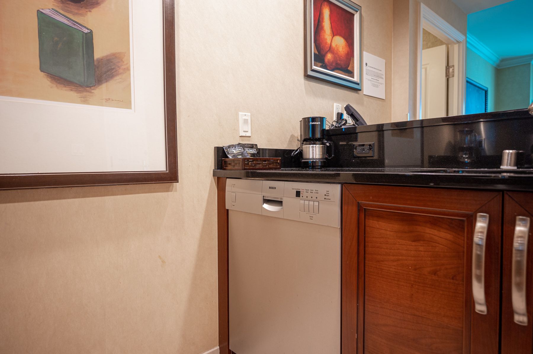 Kitchen counter with coffee maker, mini fridge, and wooden cabinets under framed wall art