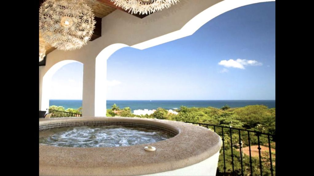 Covered patio with a round hot tub overlooking the ocean and sky