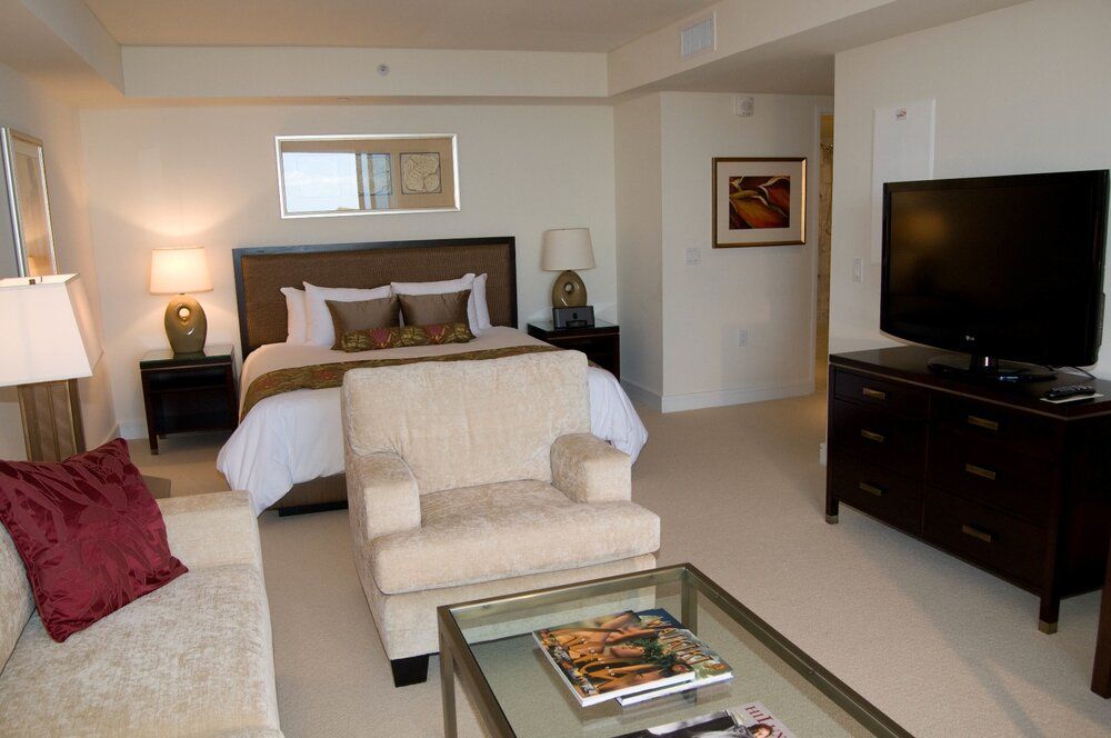 Modern hotel room with a bed, armchair, TV, and glass coffee table