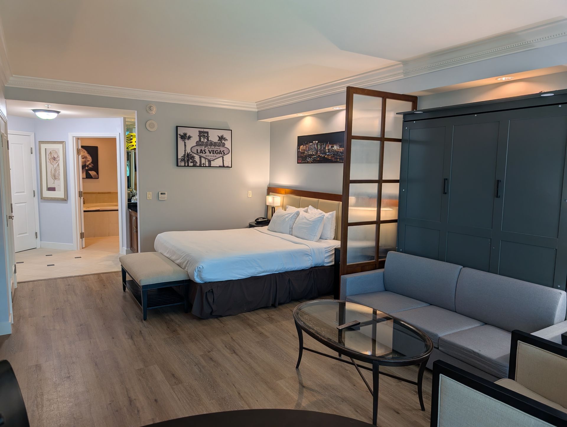 Modern bedroom with a bed, sofa, glass coffee table, and blue wardrobe in a softly lit room