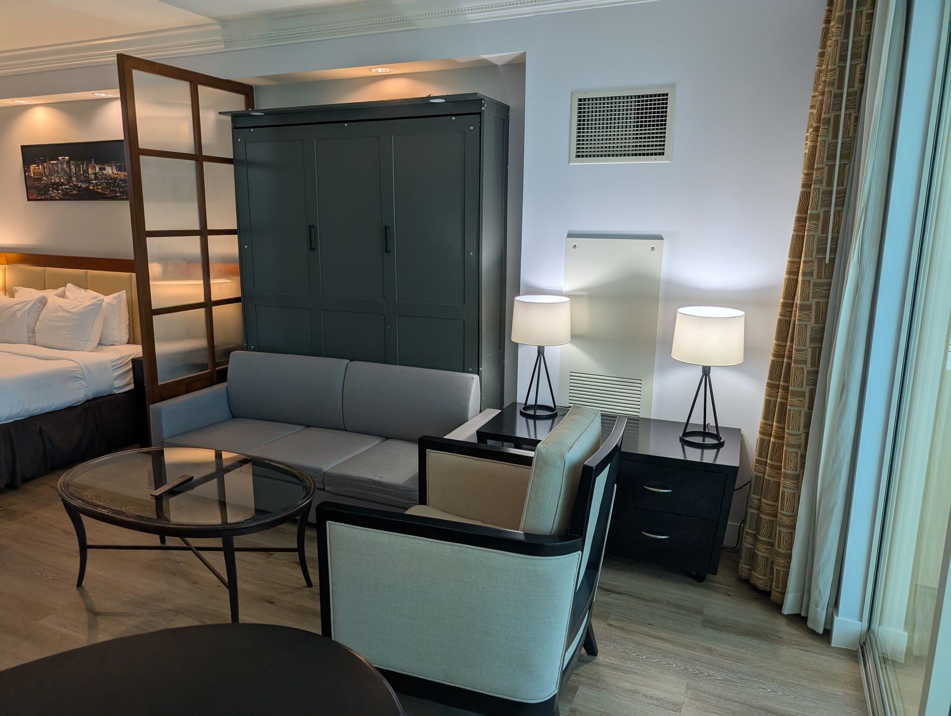 Modern hotel suite with bed, sofa, coffee table, lamps, and floor-to-ceiling curtains