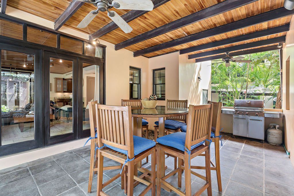 Covered patio with wooden dining table, bar stools, ceiling fans, and outdoor kitchen area