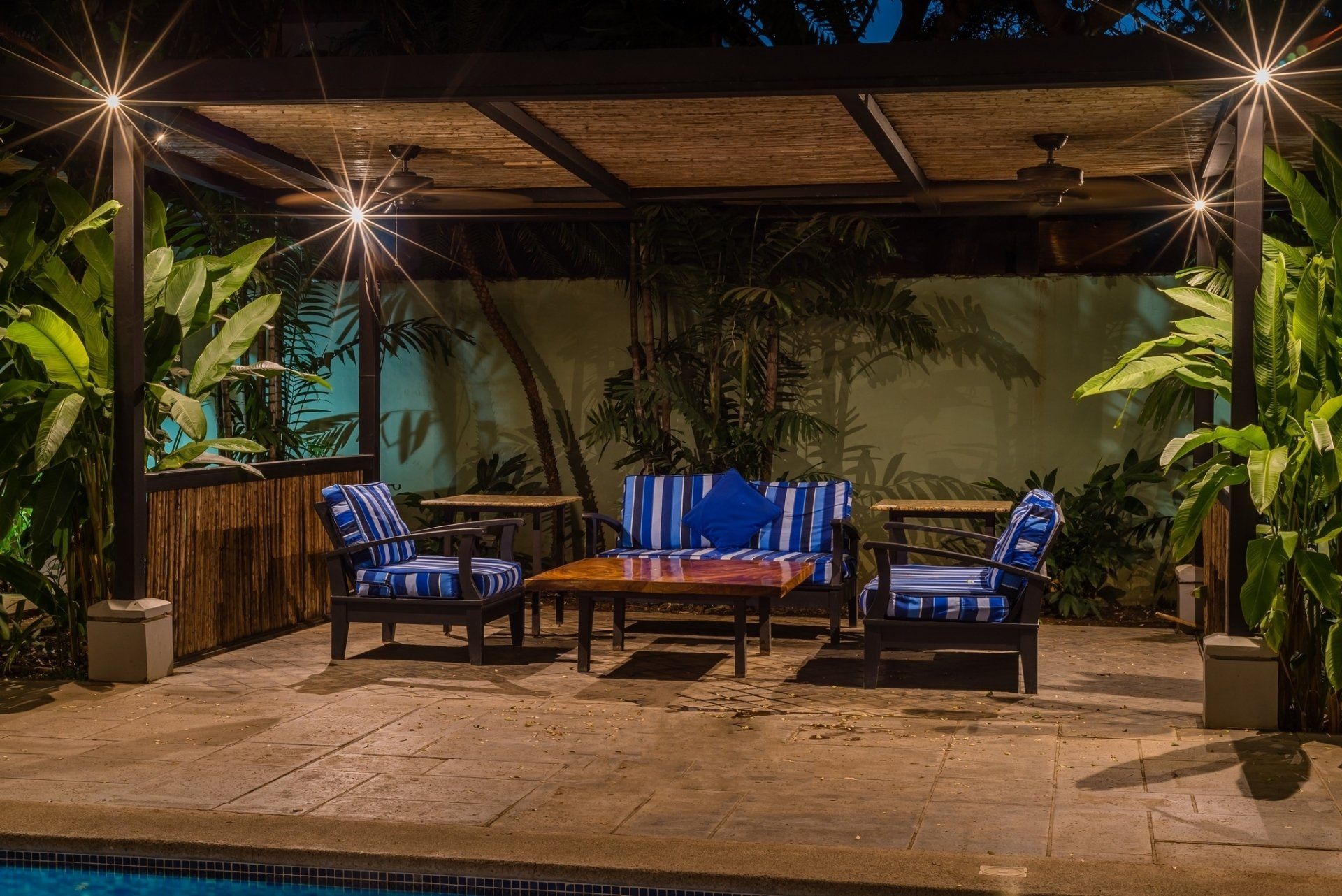 Covered patio lounge with blue chairs, coffee table, and warm string lights at night