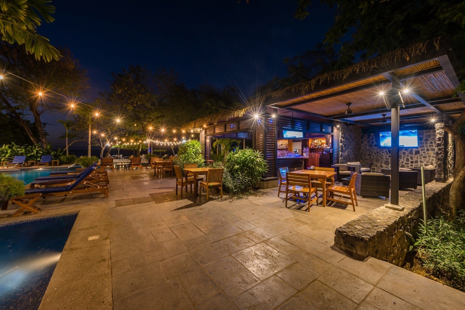 Outdoor restaurant patio at night with string lights, wooden tables, and lush greenery