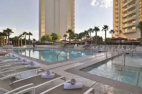 Luxury hotel pool deck with loungers, palm trees, and high-rise towers at sunset