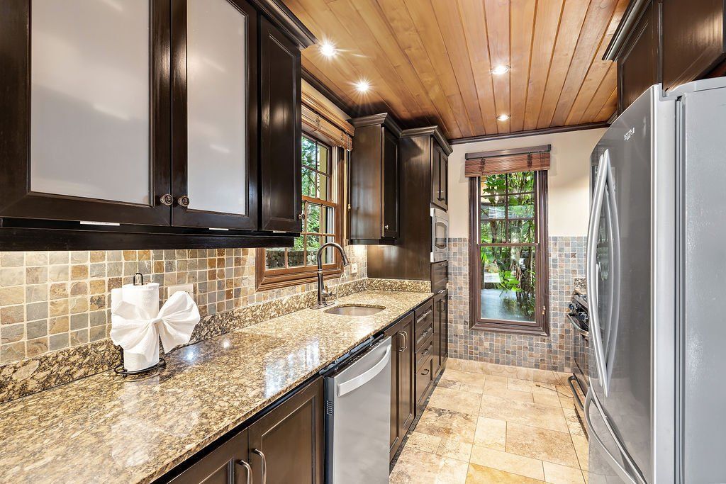 Modern kitchen with dark cabinets, granite countertops, stainless steel appliances, and a wood-paneled ceiling