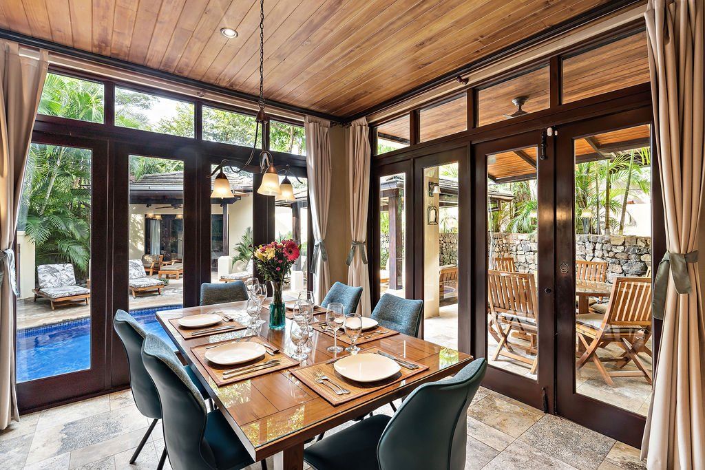 Modern dining room with wooden ceiling, glass doors, and a set table overlooking an outdoor patio.