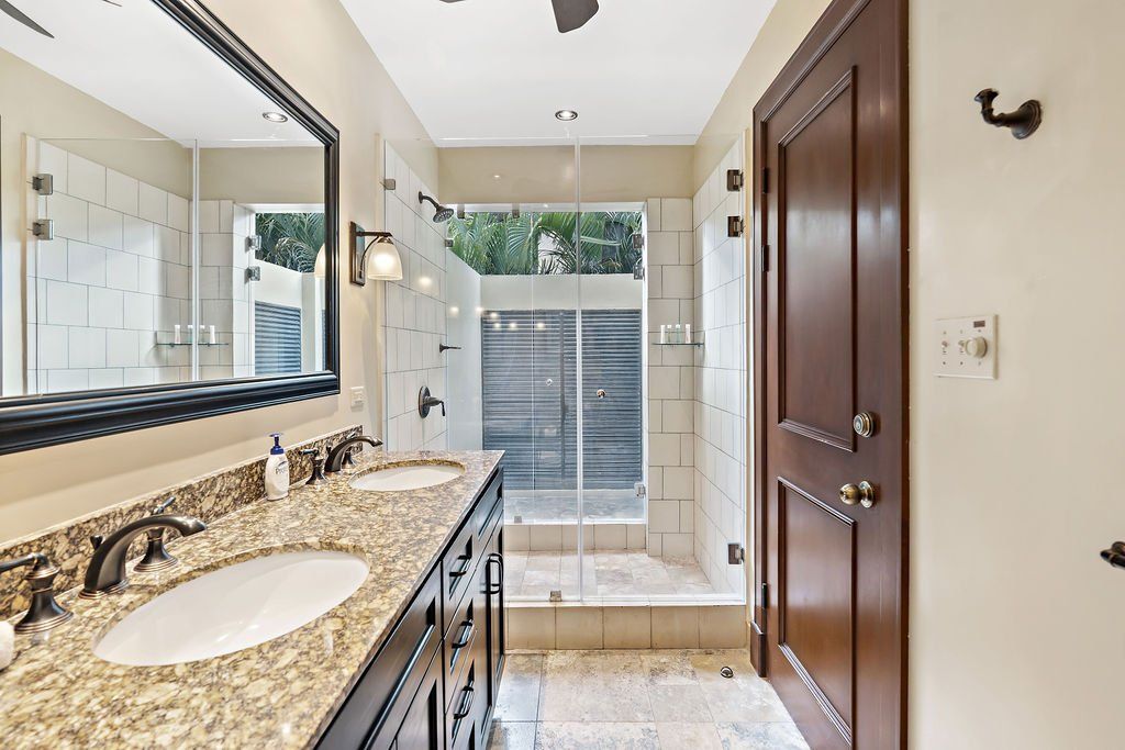 Bathroom vanity with granite countertop, large mirror, and glass shower doors by a wooden entry door