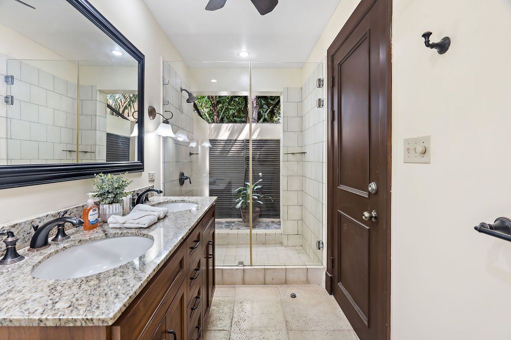 Modern bathroom with double sink vanity, large mirror, glass shower, and dark wood door.