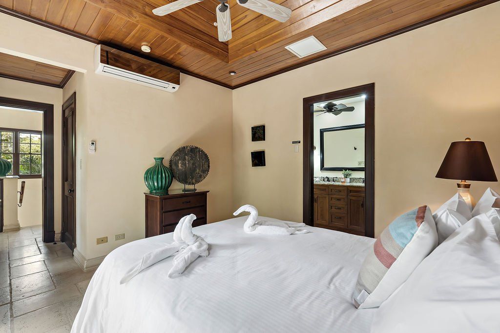 Bright bedroom with a large bed, wooden ceiling, and a doorway to a tiled bathroom.