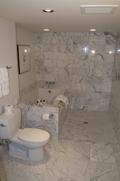 Marble bathroom with toilet, tub, and walk-in shower with glass partition