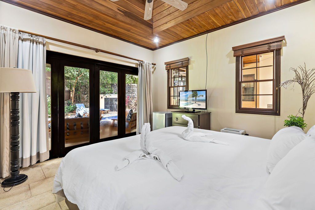Bright bedroom with white bed, wood ceiling, sliding glass doors, and a small desk by the window