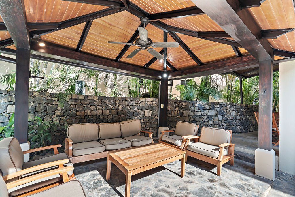 Open-air patio lounge with cushioned seating, wooden coffee table, and thatched roof