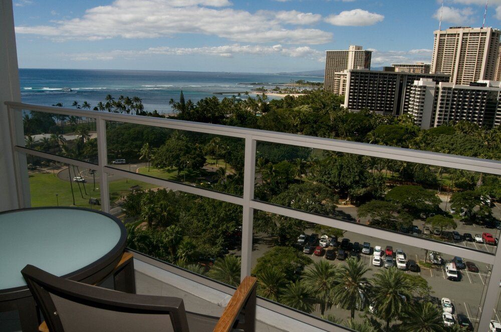 Balcony view of ocean, city skyline, and palm trees with table and chairs in foreground