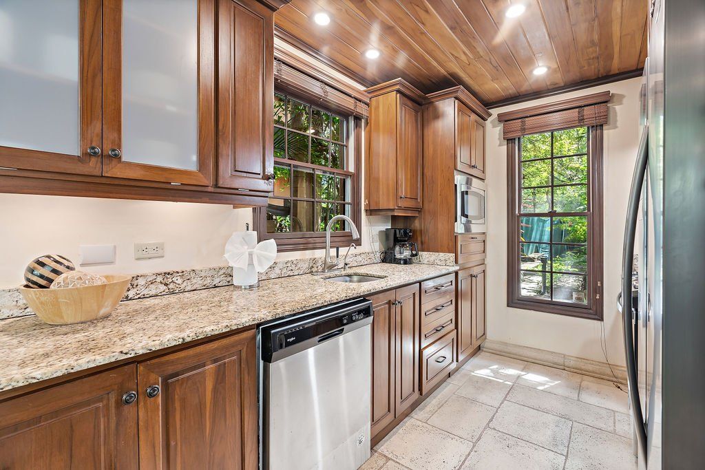 Bright kitchen with wood cabinets, granite counters, stainless dishwasher, and a glass door to greenery.