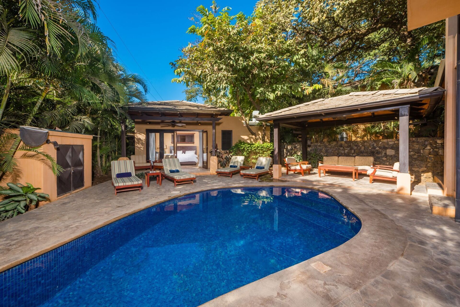 Backyard patio with blue swimming pool, lounge chairs, and shaded seating area under trees