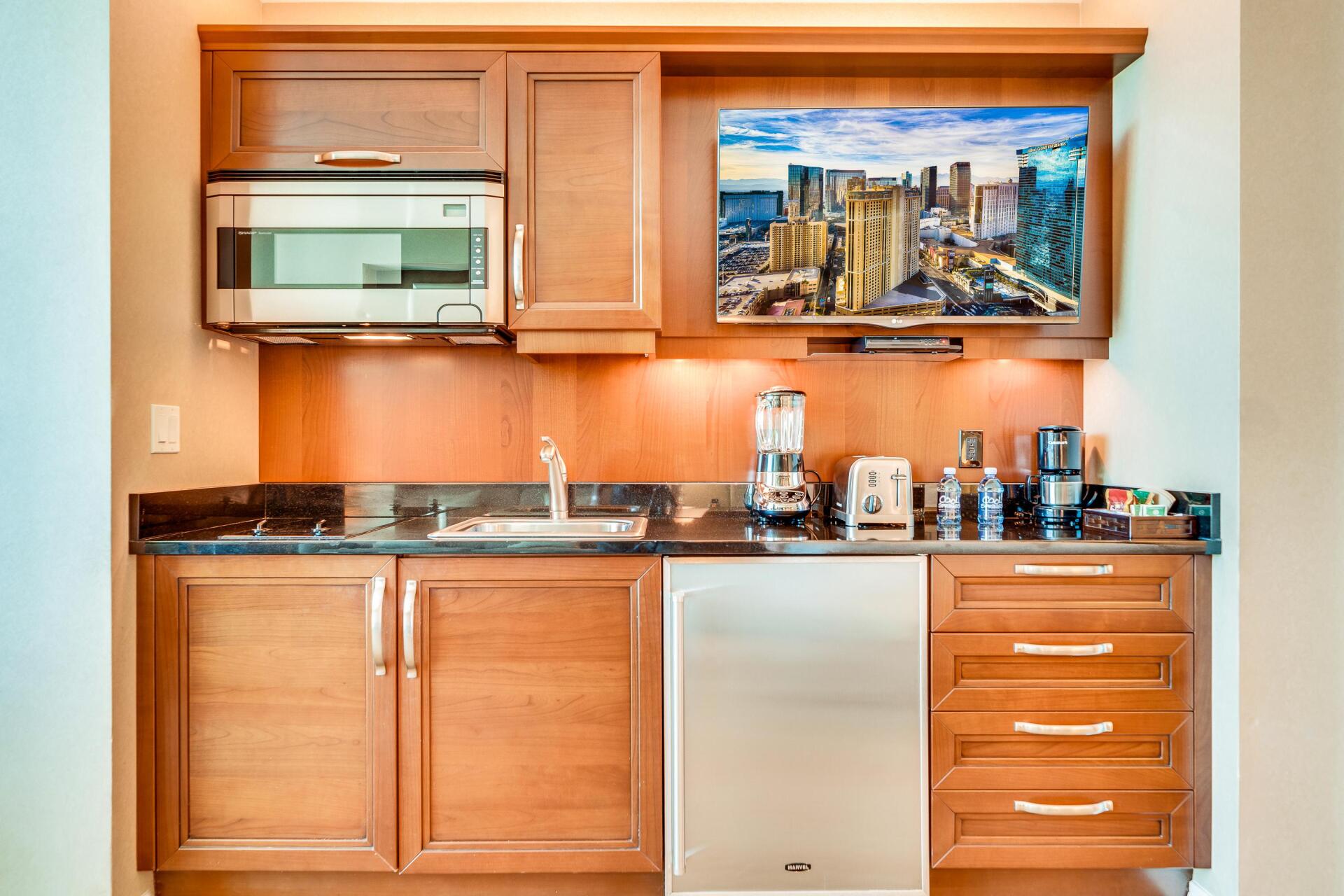 Wood-paneled kitchenette with sink, mini fridge, coffee maker, and wall art above the counter.