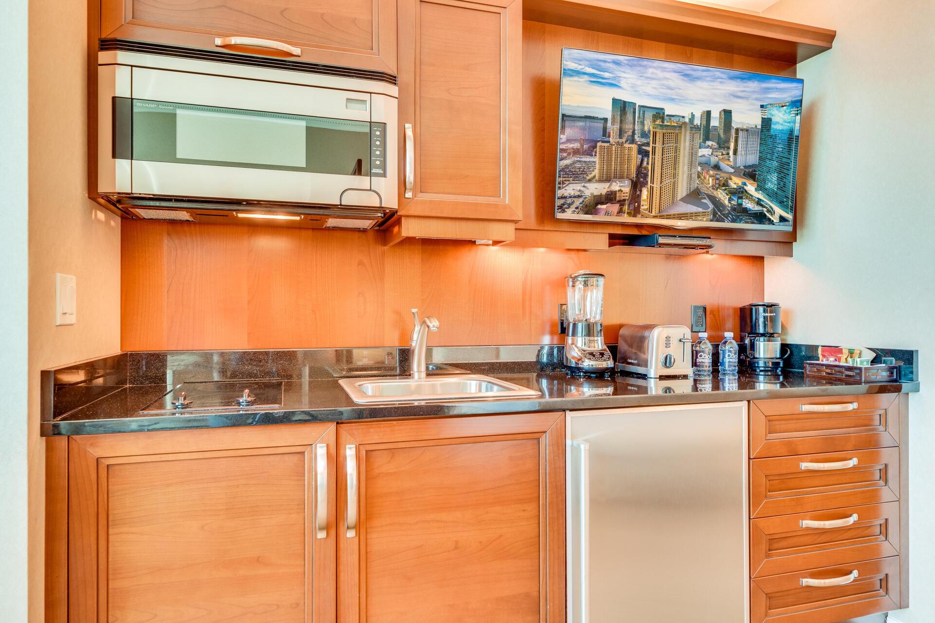 Wooden kitchenette with microwave, sink, mini fridge, cabinets, and countertop decor