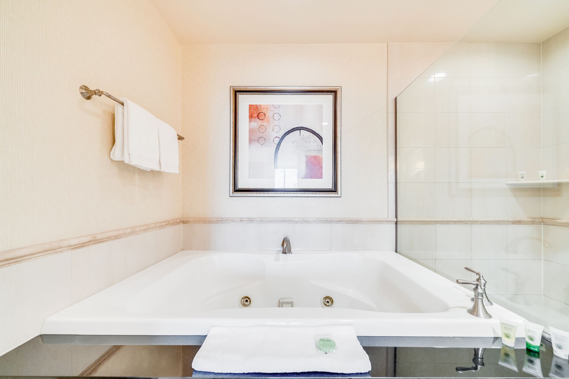 Bright bathroom with a white corner bathtub, towel rack, and framed wall art.