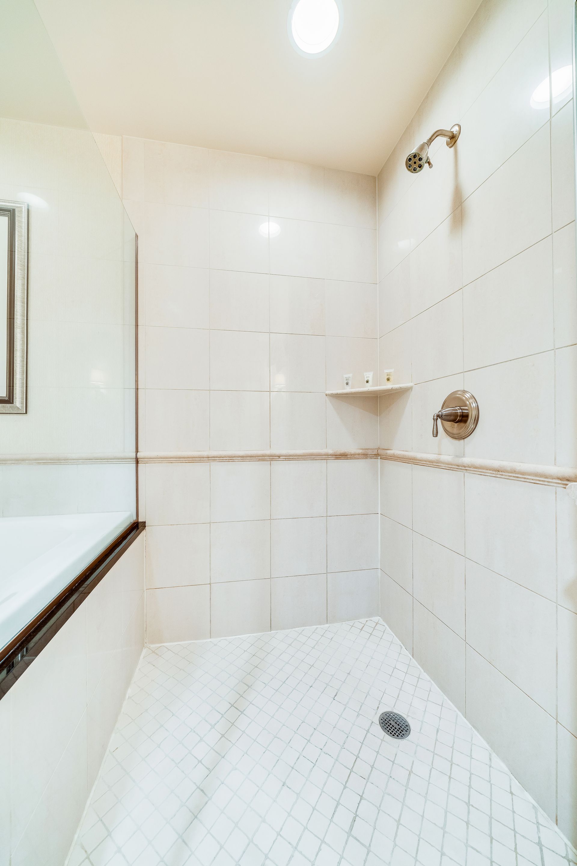 White tiled shower stall with built-in shelves, chrome fixtures, and a sloped shower floor