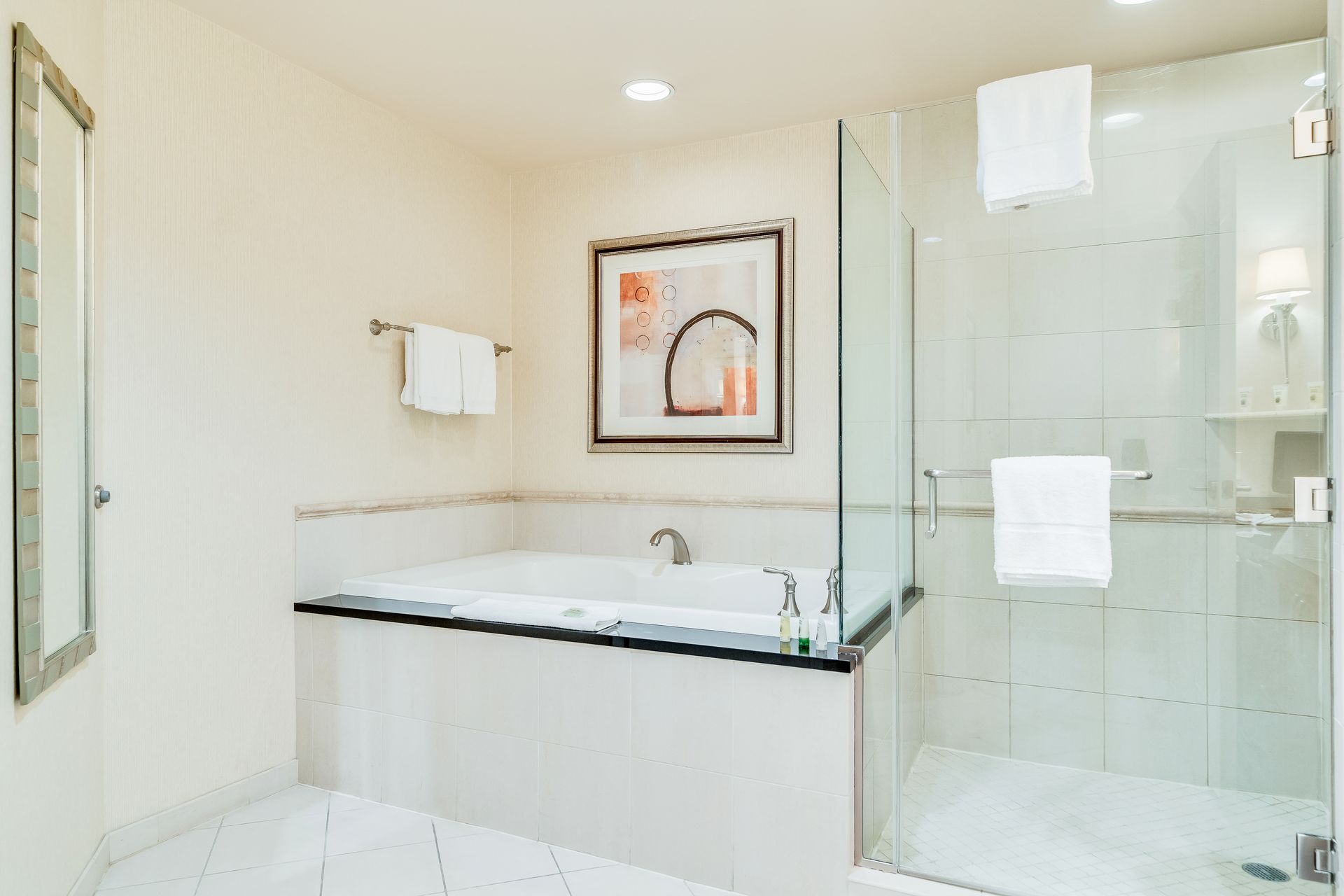 Bright modern bathroom with a white soaking tub, glass shower, and framed wall art.