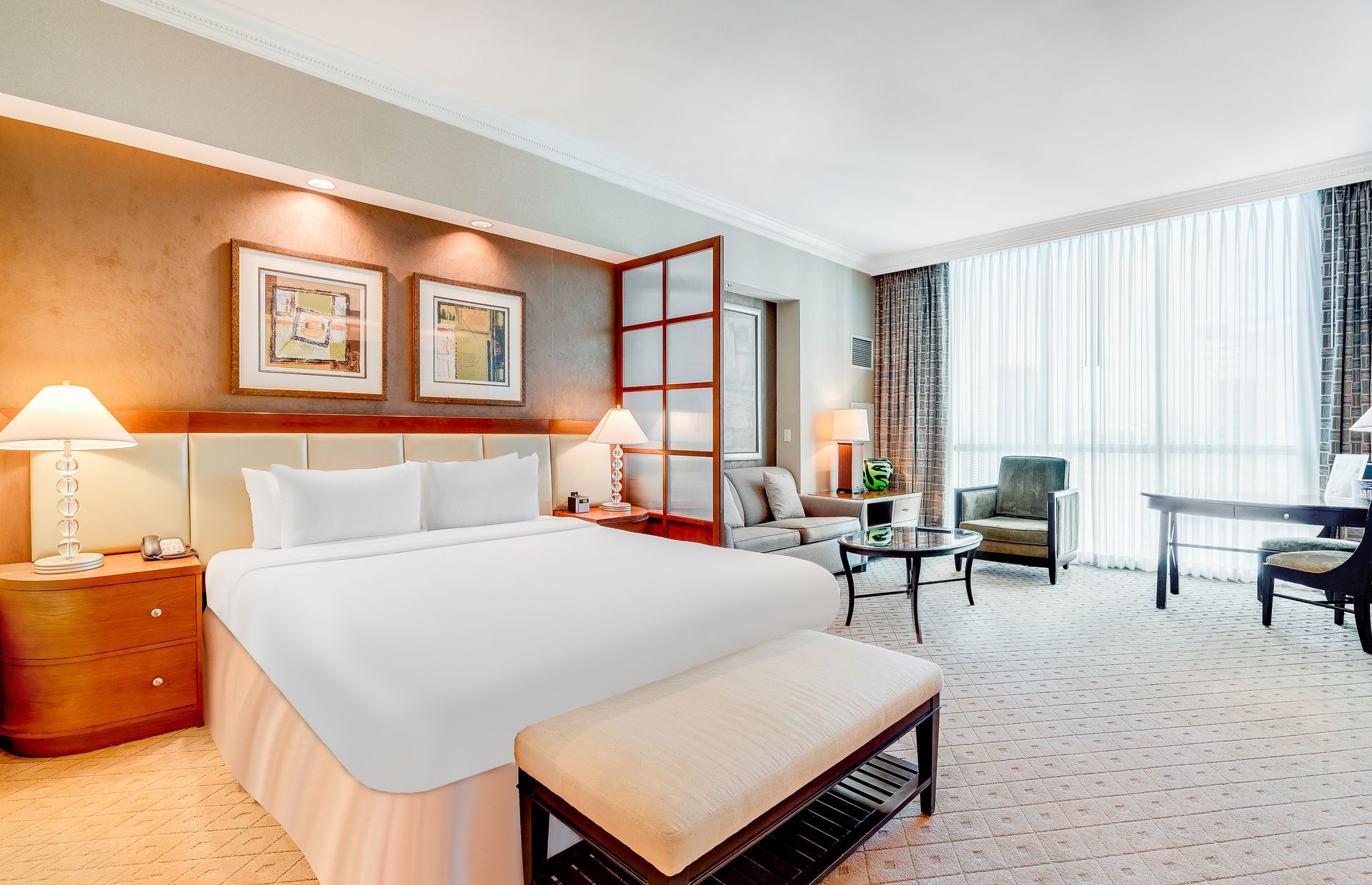 Modern hotel room with king bed, sofa, desk, and bright window seating area