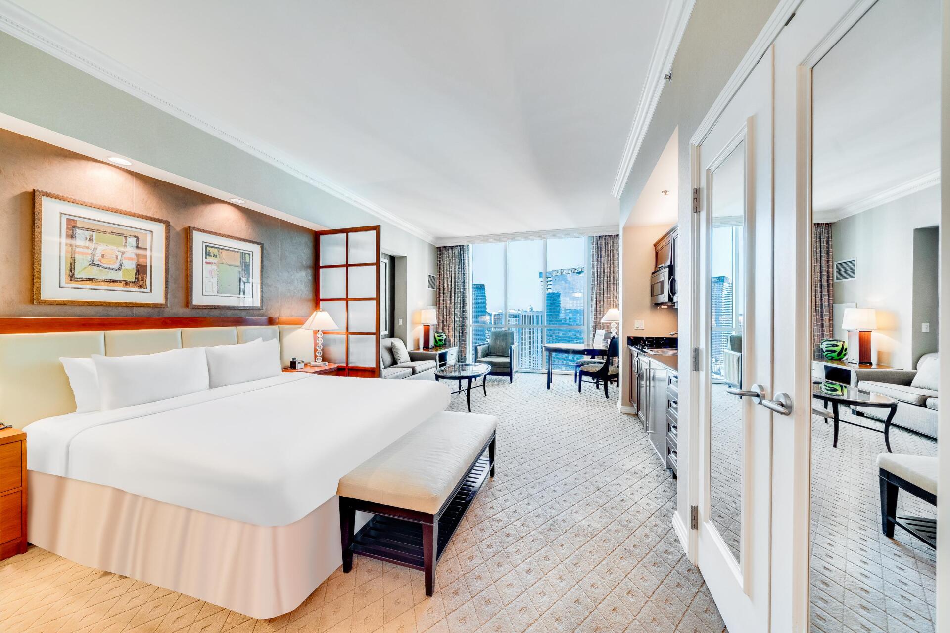 Bright hotel room with a large bed, mirrored closet, desk, and city view through the windows.