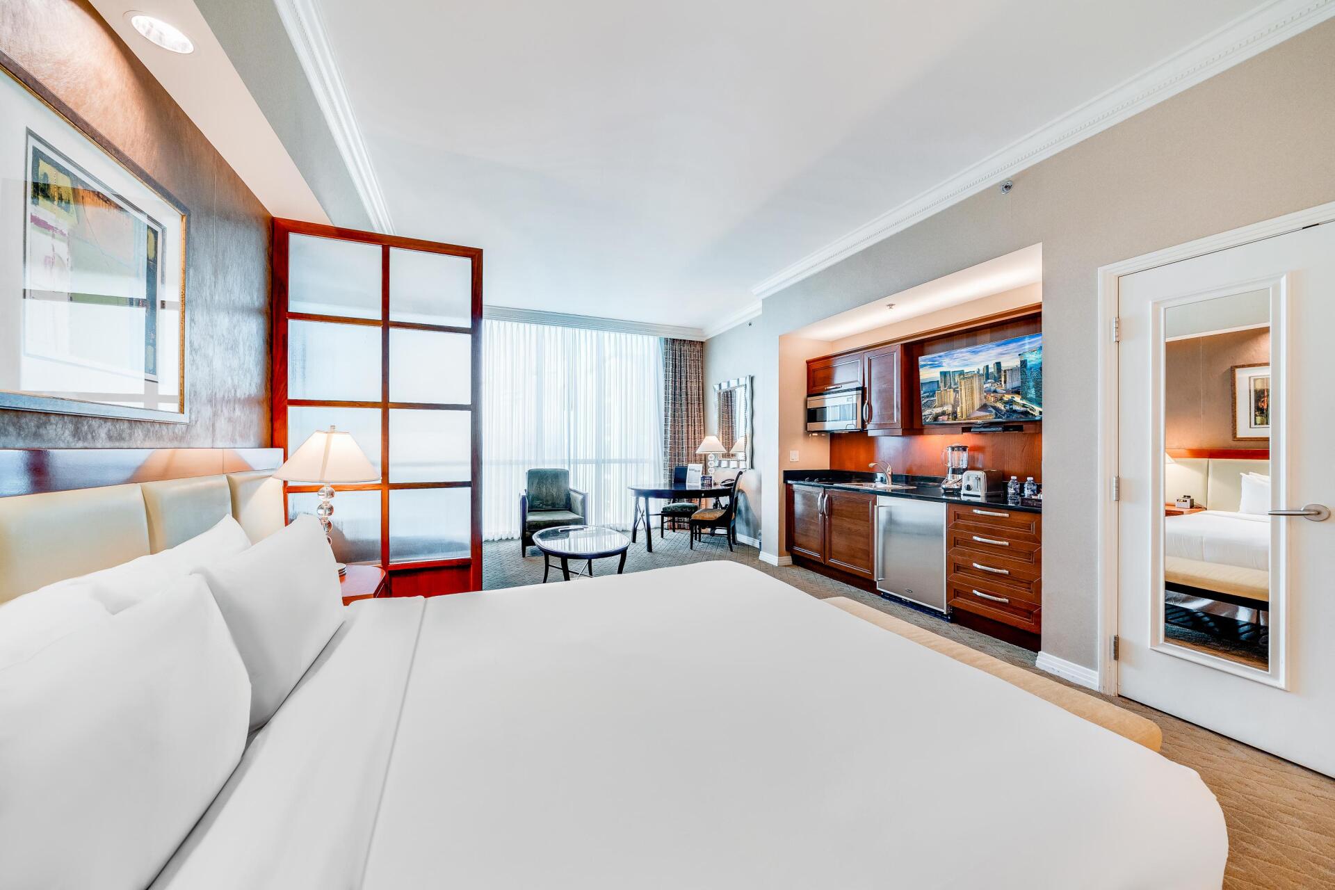Modern hotel room with a large bed, desk, wooden minibar, and bright windows