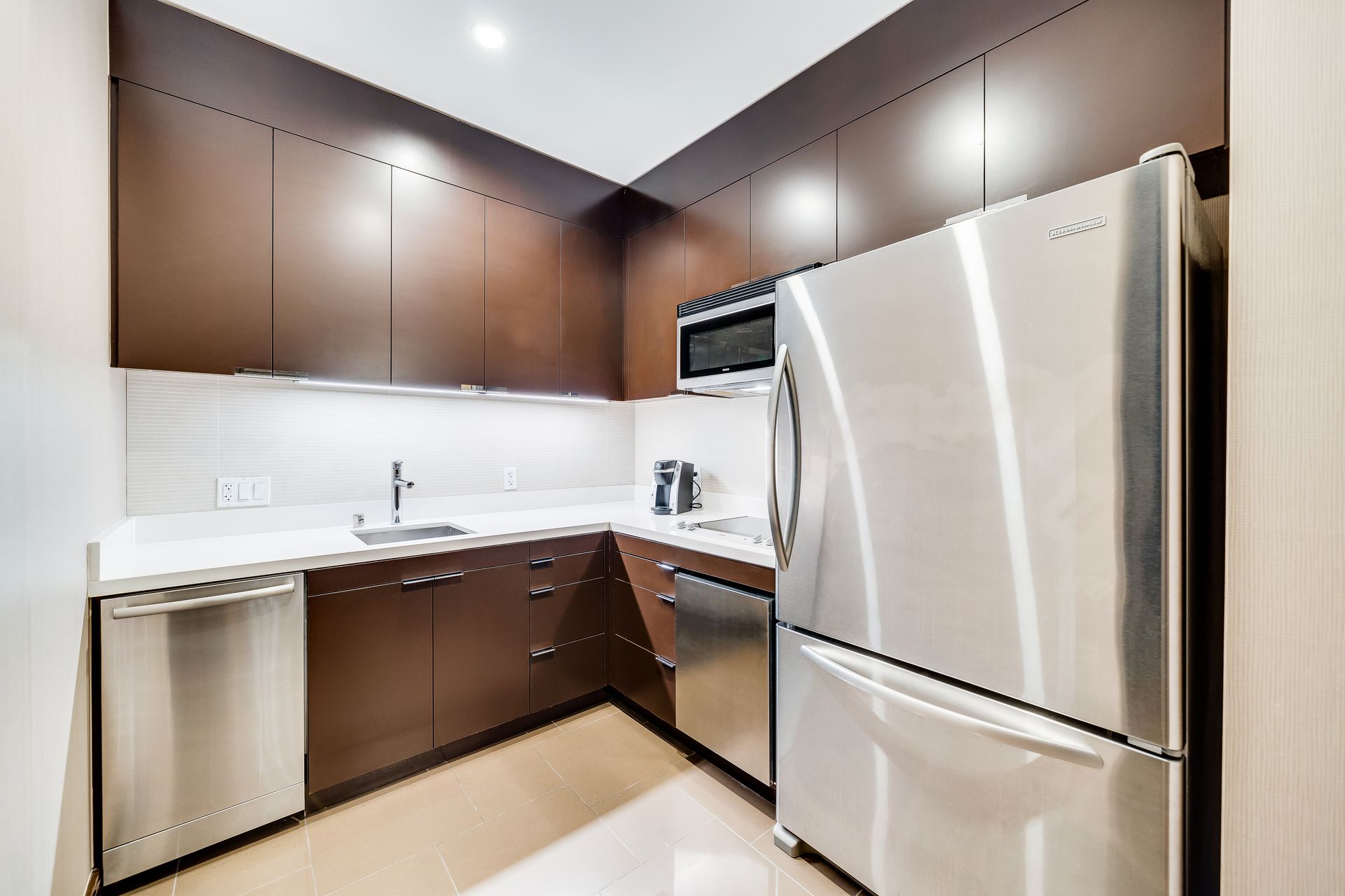 Modern kitchen with dark brown cabinets, stainless steel appliances, and white countertops.