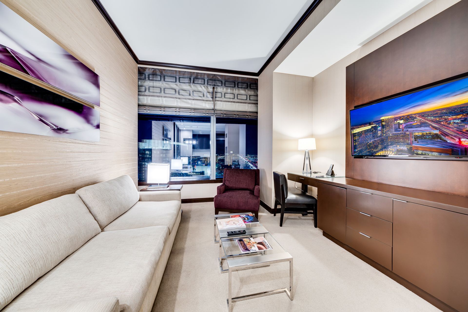 Modern living room with beige sofa, burgundy chair, desk lamp, and colorful cityscape wall art
