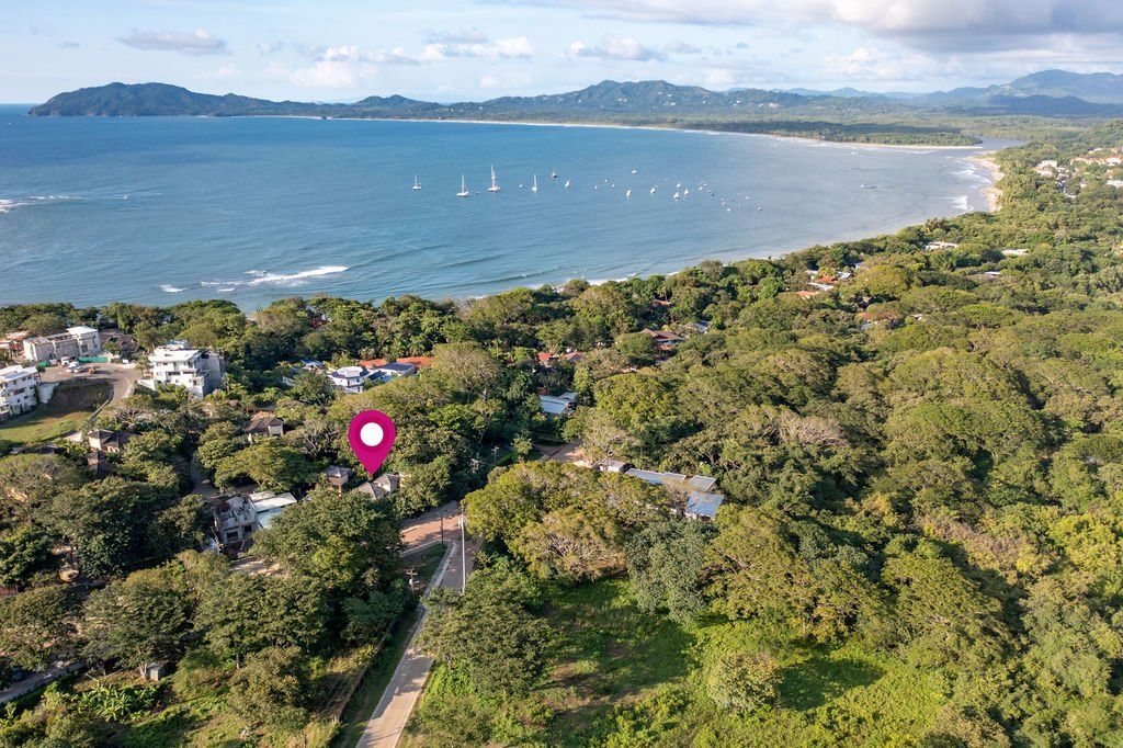 Aerial view of a tropical bay with a beach, sailboats, and dense green coastline.
